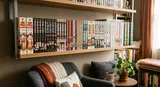 間接照明が灯るモダンな棚に並ぶ、多種多様なマンガ本。居心地の良い読書コーナーには椅子と観葉植物が配され、全体が温かみのある色調と鮮やかな表紙の色合いで彩られています。